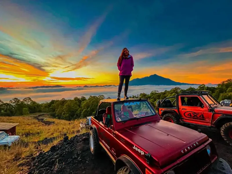 Red jeeps and a visitor at a sunrise viewpoint above the clouds