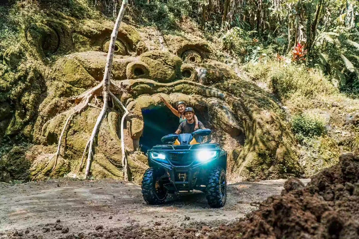 Helmeted driver and passenger on a 450cc ATV in front of Gorilla Cave