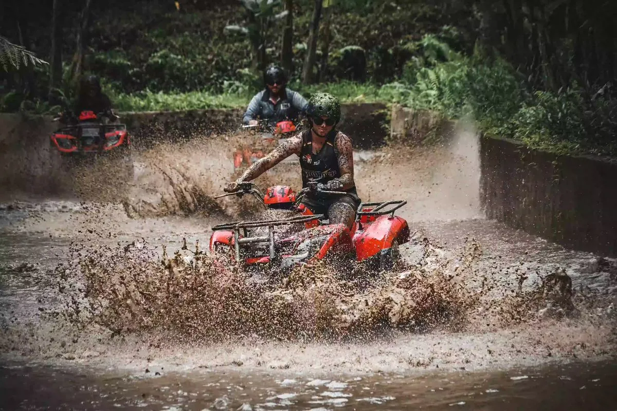 Helmeted rider on a red ATV splashing through a muddy trail at Alasan Adventure