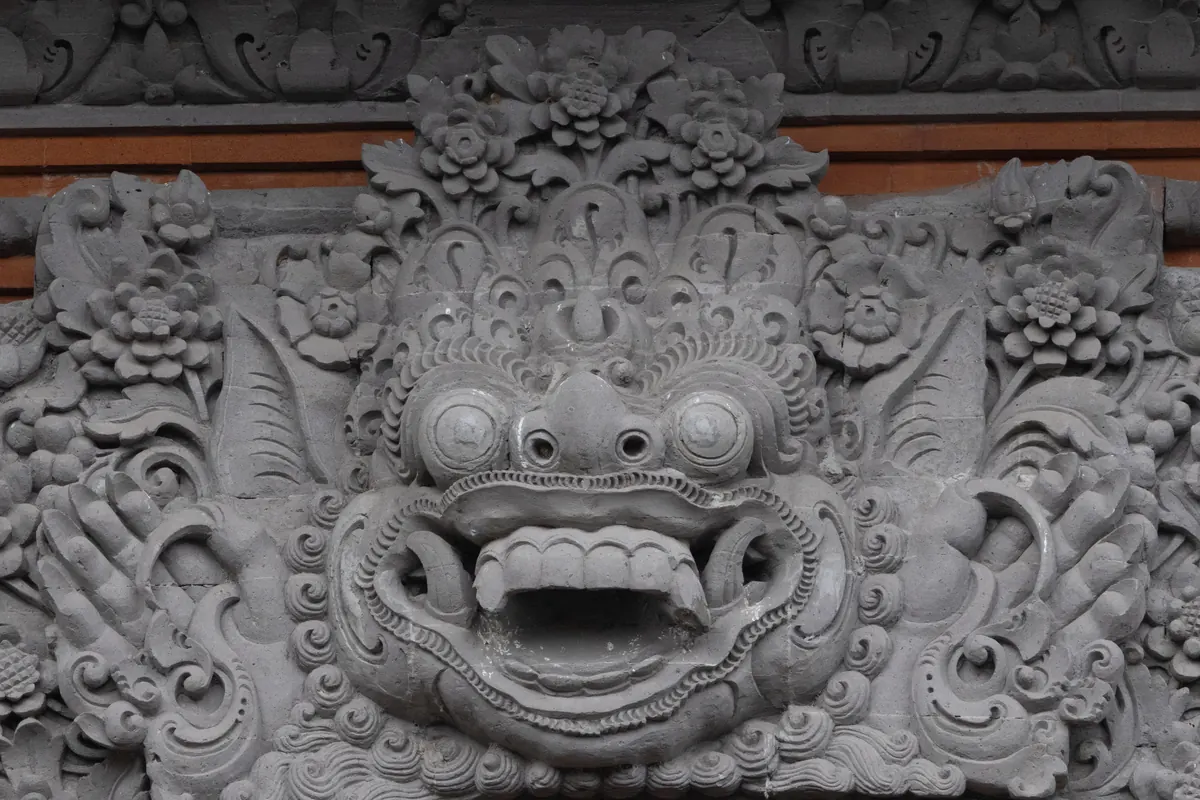 Close view of a carved Karang Boma face and floral stonework at Bale Banjar Ubud Kelod.